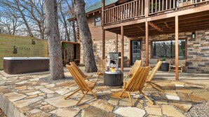 Eine Terrasse mit Steinfliesen, Holzstühlen, einer Feuerstelle und einem Whirlpool.