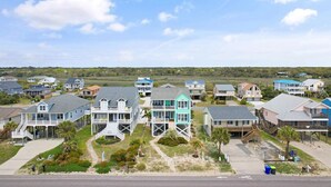A coastal residential area with houses featuring balconies, some with attached decks, and a clear view of the beach in the background. - Oceanview Key Rest on Oak Island: Spacious 6BR, 5BA home for 15 guests with pool. (Oak Island)