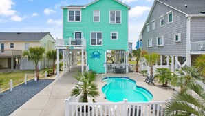 A two-story building with a pool, surrounded by a white fence, palm trees, and a clear sky. - Oceanview Key Rest on Oak Island: Spacious 6BR, 5BA home for 15 guests with pool. (Oak Island)