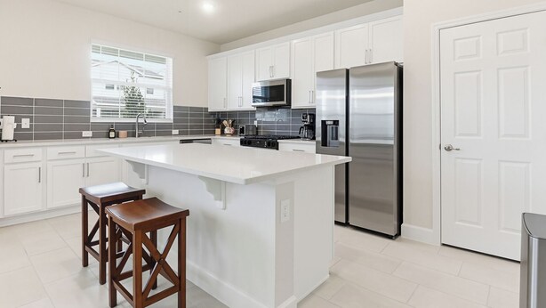 Una cocina moderna con armarios blancos, un refrigerador de acero inoxidable, un microondas y una isla grande con taburetes.