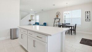 Una cocina moderna con armarios blancos, una isla central y un comedor con mesa y sillas.
