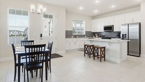 Una cocina moderna con armarios blancos, un refrigerador de acero inoxidable y un comedor con mesa y sillas.