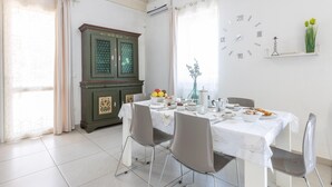 Een eethoek met een tafel gedekt voor vier personen, een groen kastje, een wandklok en een raam met gordijnen.