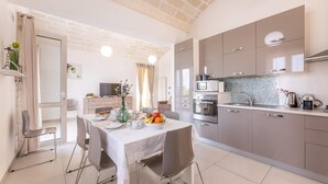 Een moderne keuken met een eethoek, met een bakstenen plafond, roestvrijstalen apparatuur en een witte tafel gedekt met een fruitschaal.