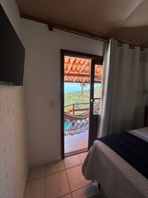 Una habitación con una cama, una puerta que da a un balcón con vistas al mar y una hamaca.