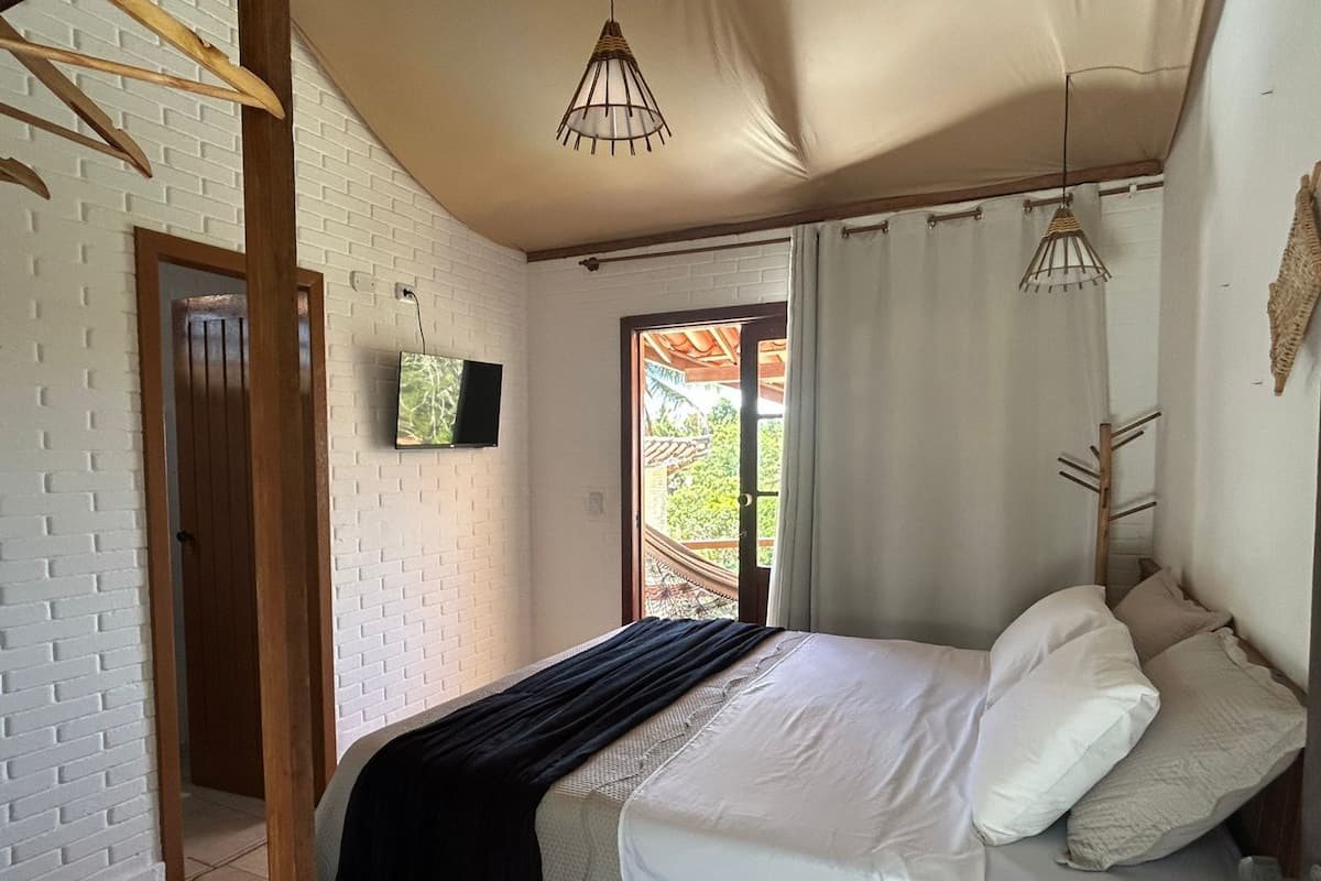 A bedroom with a bed, a television, and a view of the outdoors.