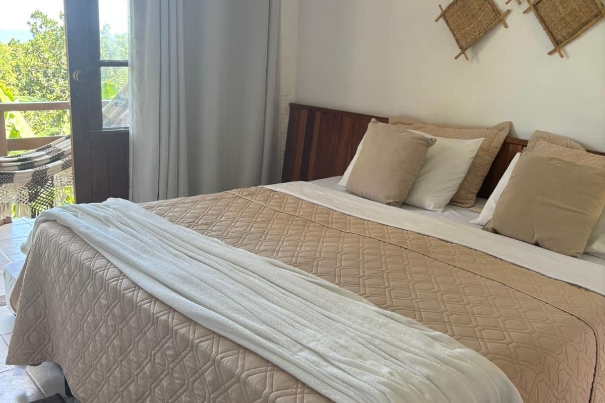 A bedroom with a bed, a view of greenery outside, and a door.