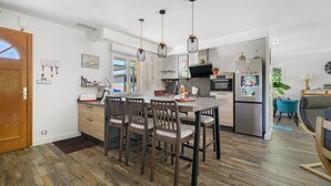 Eine moderne Küche mit Holzboden, einem Esstisch mit Stühlen, Pendelleuchten und einem Kühlschrank.