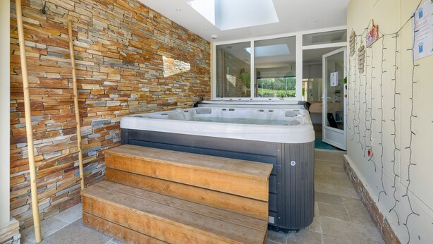 Ein Whirlpool in moderner Outdoor-Umgebung mit Steinwand, Holzstufen und einem Oberlicht.