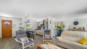 Ein geräumiger Wohnbereich mit einer Couch, Sesseln, einem Esstisch und einer Küche im Hintergrund.