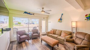 Ein Wohnzimmer mit einer Couch, zwei Sesseln, einem Couchtisch, einem Deckenventilator und Blick durch ein großes Fenster.
