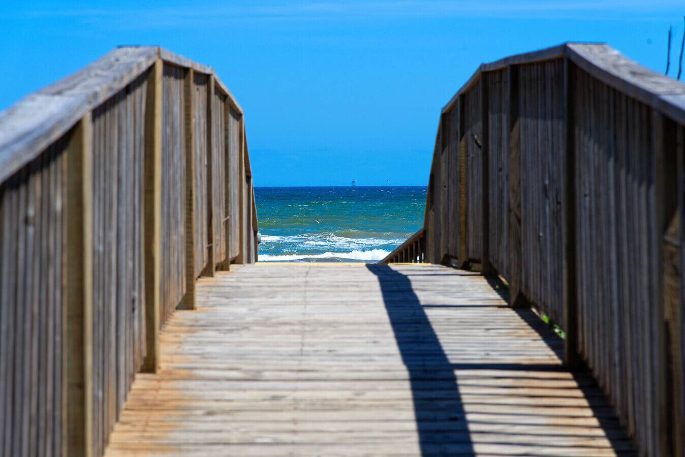 A wooden boardwalk leading to the ocean with clear skies.