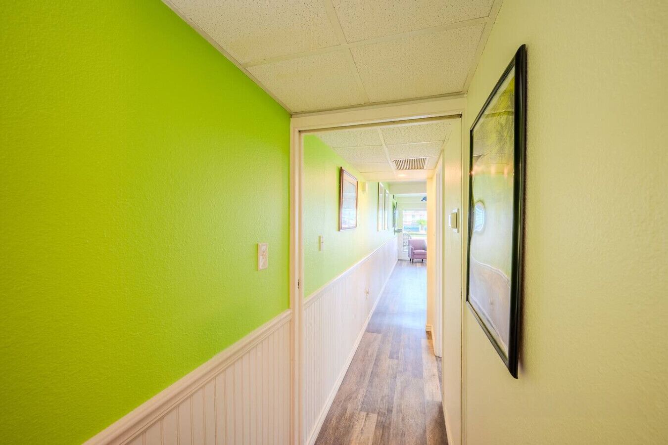 Un couloir avec un mur vert, des lambris blancs et un plancher en bois.