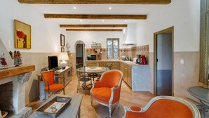 A cozy living room with a fireplace, orange chairs, a dining table, and a kitchen in the background. - Holiday Home 'Missia' with Mountain View, Wi-Fi and Air Conditioning (Porto-Vecchio)