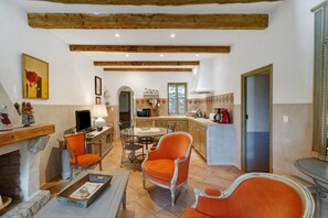 A cozy living room with a fireplace, orange chairs, a dining table, and a kitchen in the background. - Holiday Home 'Missia' with Mountain View, Wi-Fi and Air Conditioning (Porto-Vecchio)