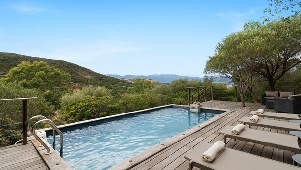 A wooden deck with a swimming pool, lounge chairs, and a view of the hills. - Holiday Home 'Missia' with Mountain View, Wi-Fi and Air Conditioning (Porto-Vecchio)