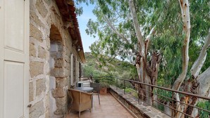 A stone building with a balcony, outdoor seating, and a view of trees and hills. - Holiday Home 'Missia' with Mountain View, Wi-Fi and Air Conditioning (Porto-Vecchio)
