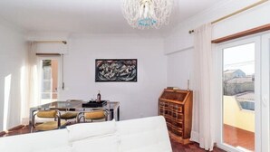 Ein Wohnzimmer mit einem weißen Sofa, einem Esstisch mit Stühlen, einer Chandelüster und einem Bild an der Wand.
