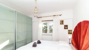 Ein Schlafzimmer mit Bett, einem fensterbepflanzten Fenster, einer Chandelieber und einem rot gepolsterten Kopfteil.