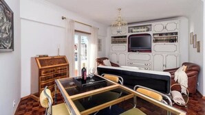 Ein Zimmer mit Esstisch mit Glasplatte, einem Fernseher, einem Bücherregal und einer Couch.