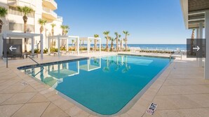 En swimmingpool med fri utsikt över havet, omgiven av palmer och en byggnad med balkonger.