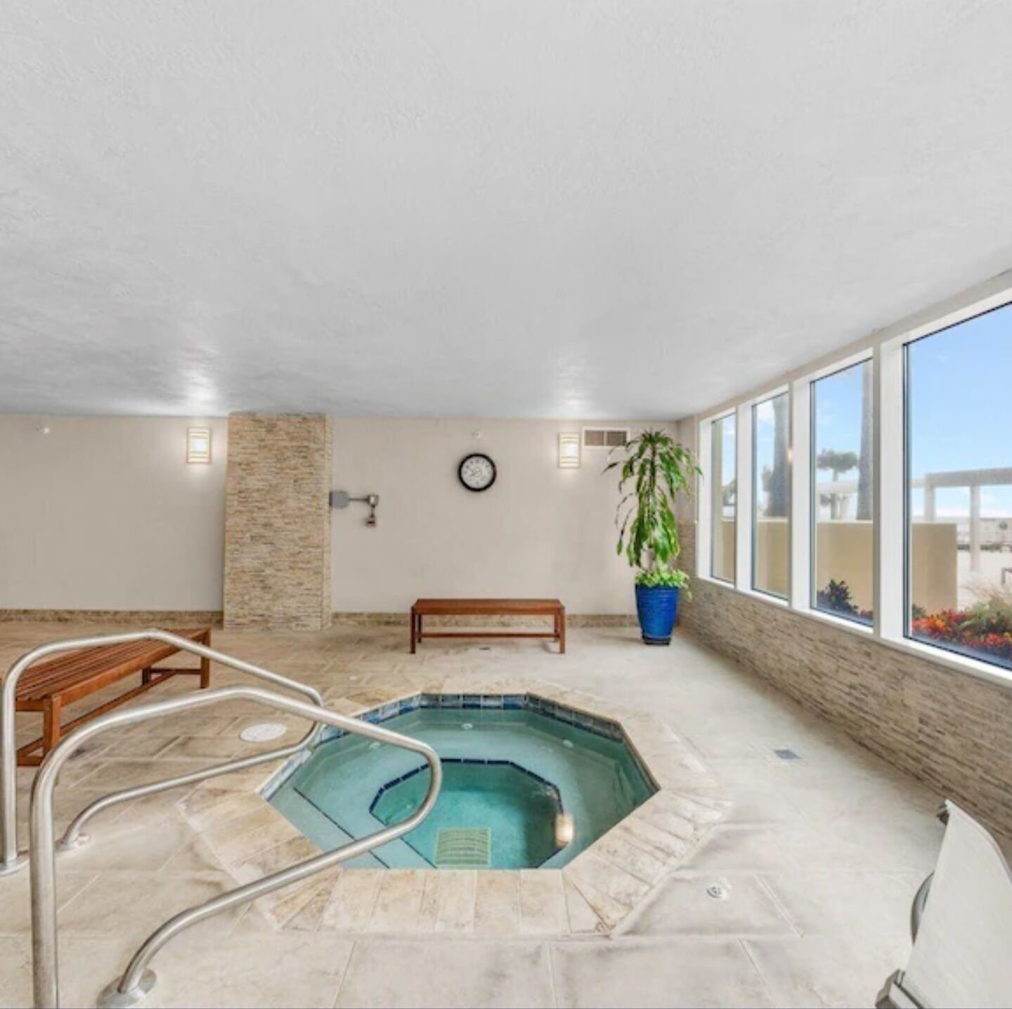 Una piscina interior con un banco de madera, un reloj en la pared y una planta en maceta.