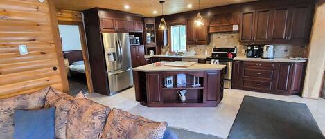 Interior de una cabaña de madera con kitchenette, un sofá y una zona de comedor.