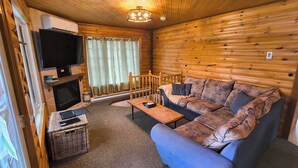 Interior de una cabaña de troncos con sofá, televisión, chimenea y una cesta de mimbre.