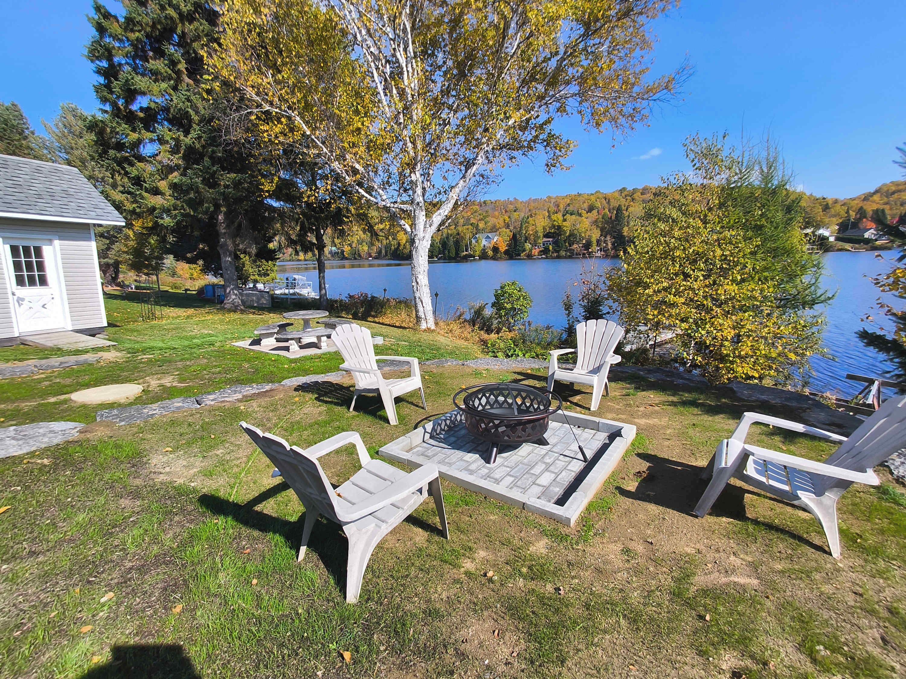 Un espace extérieur aménagé au bord du lac, avec des chaises Adirondack et un foyer.