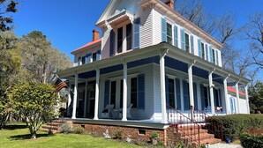 A two-story house with a porch, brick foundation, and a red roof.