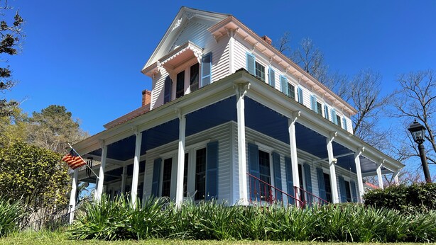 A large, two-story house with a porch, columns, and a flag.