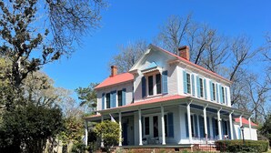 A large, two-story house with a red roof, white siding, and blue shutters.
