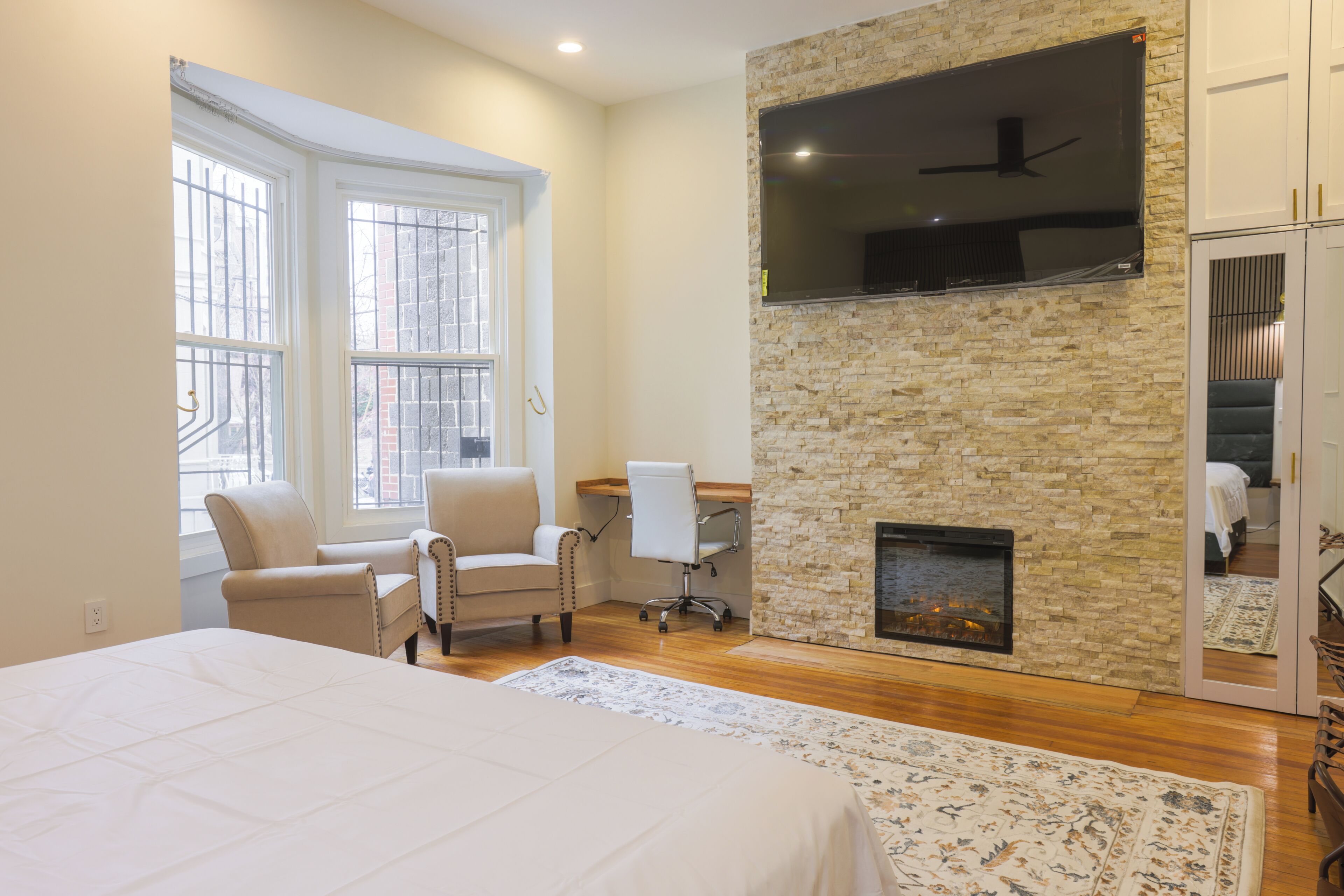 Un dormitorio con una cama grande, una chimenea, un televisor montado en una pared de piedra y un escritorio con una silla.