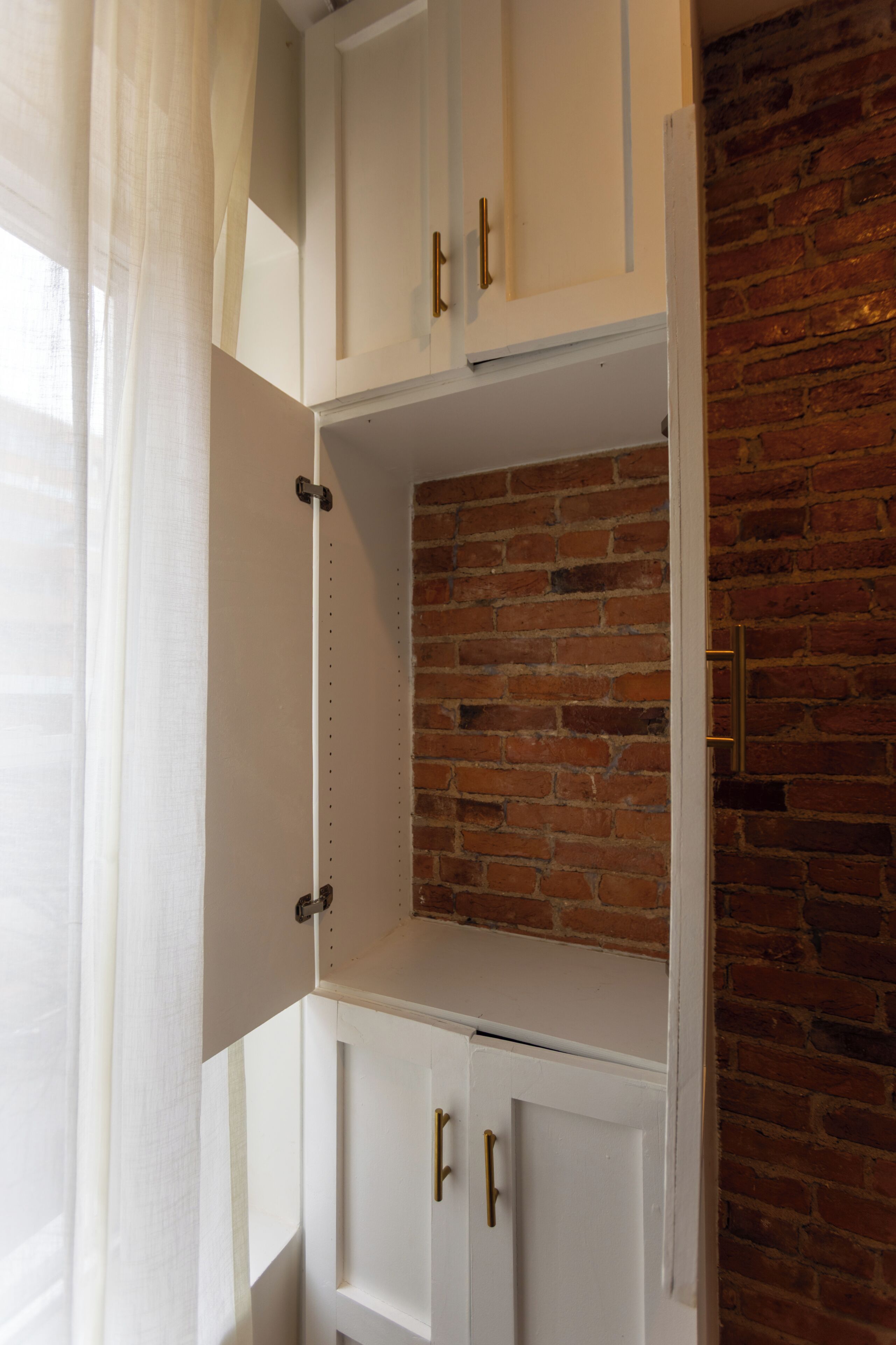Un meuble de rangement blanc avec des poignées en métal, un mur en briques et une porte blanche.