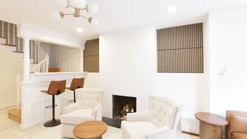 A modern living room with a fireplace, white furniture, and a staircase.