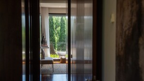 Ein Flur, der zu einem Balkon mit Blick auf Bäume, einem weißen Stuhl und einem Tisch führt.
