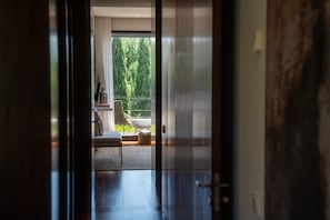 Un couloir menant à un balcon d’où l’on peut admirer les arbres, avec une chaise blanche et une table.