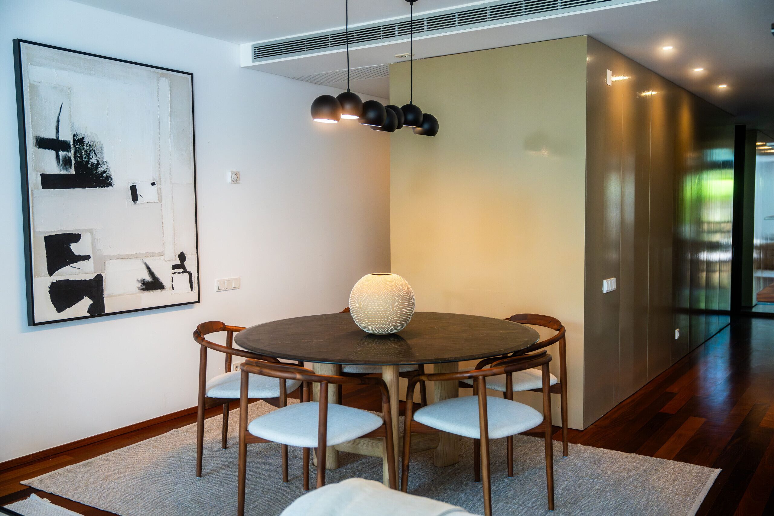 Un comedor moderno con una mesa redonda, sillas, un florero y una lámpara de pared.