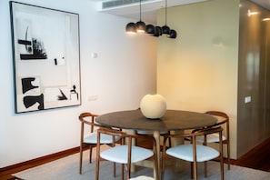 A dining area with a round table, six chairs, a large abstract painting, and pendant lighting.