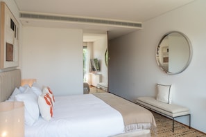 A hotel room with a bed, bedside table, chair, and a round mirror on the wall.