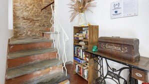 Un escalier avec des murs en pierre, une bibliothèque en bois et une machine à coudre ancienne.
