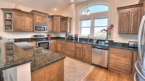 A kitchen with wooden cabinets, granite countertops, stainless steel appliances, and a large window. - Experience ocean views in this spacious 4-bed, 3-bath home on Oak Island. (Oak Island)