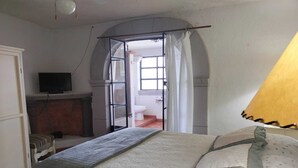 A bedroom with a bed, a television, a fireplace, and an open door leading to another room. - Casa Encanto Santa Noche  (San Miguel de Allende)