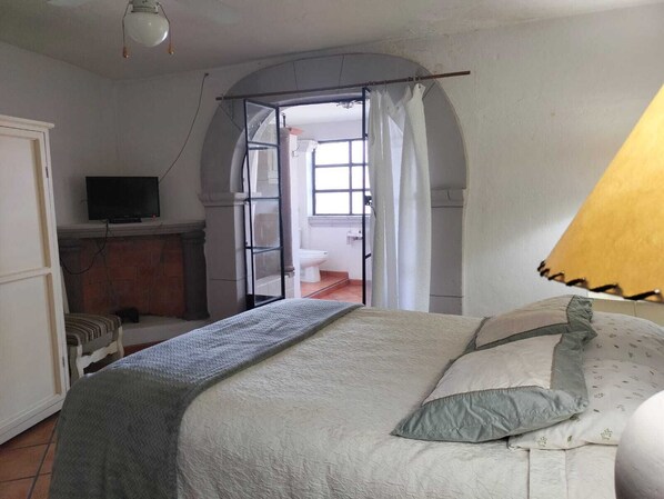 Un dormitorio con cama, televisor, chimenea y puerta abierta que da a otra habitación.