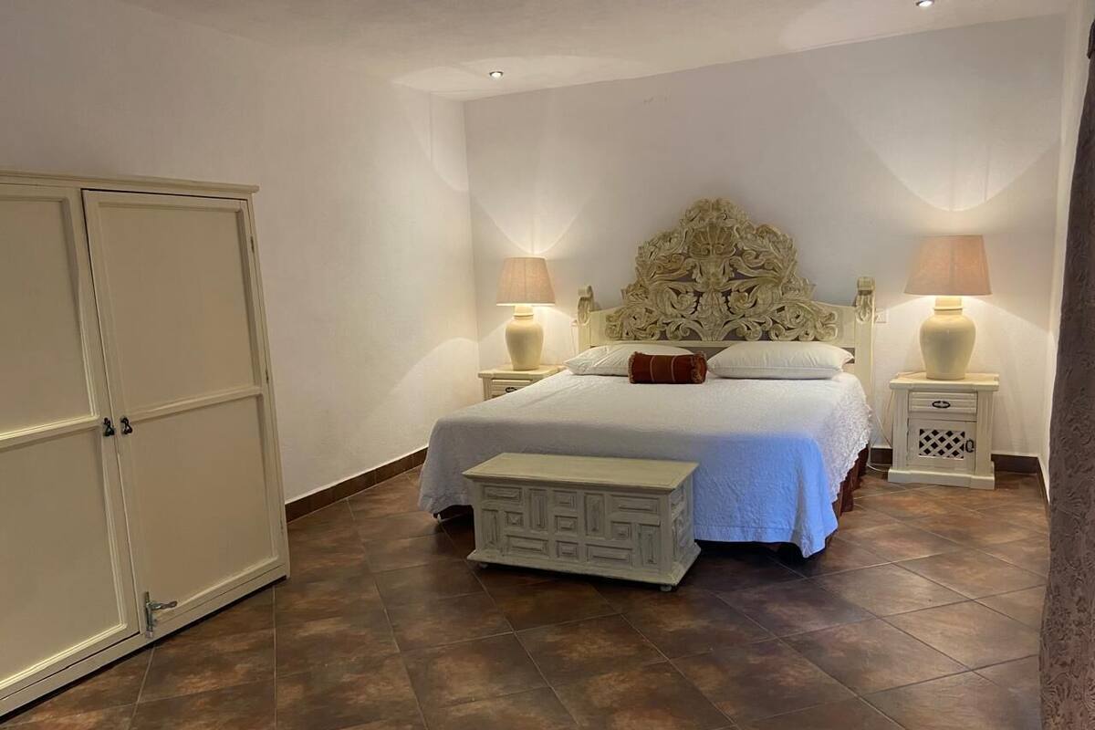 Una camera da letto con un letto, lampade ai comodini, un comodino, un armadio e una panca.