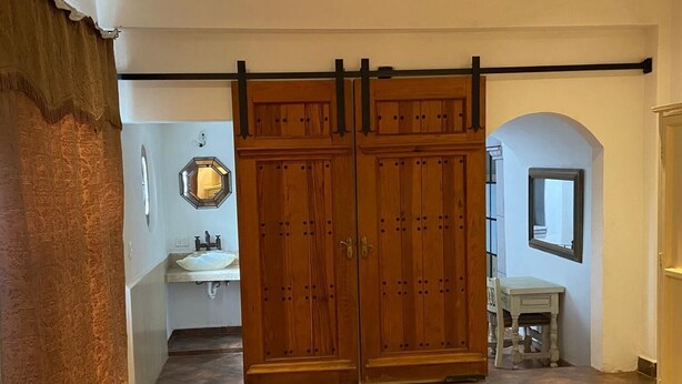 A room with a double door, a sink, a mirror, and a small table. - Casa Encanto Santa Noche  (San Miguel de Allende)