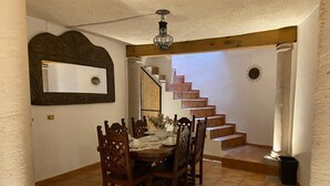 A dining area with a wooden table and chairs, a staircase, and a decorative mirror on the wall. - Casa Encanto Santa Noche  (San Miguel de Allende)