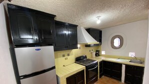 A compact kitchen with dark cabinets, a white refrigerator, a stove, and a sink. - Casa Encanto Santa Noche  (San Miguel de Allende)