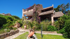 Un edificio in pietra con un balcone, immerso nel verde e decorato con piante in vaso.