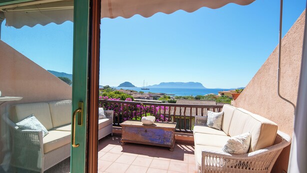 Un balcone con mobili in vimini, vista sul mare e montagne in lontananza.